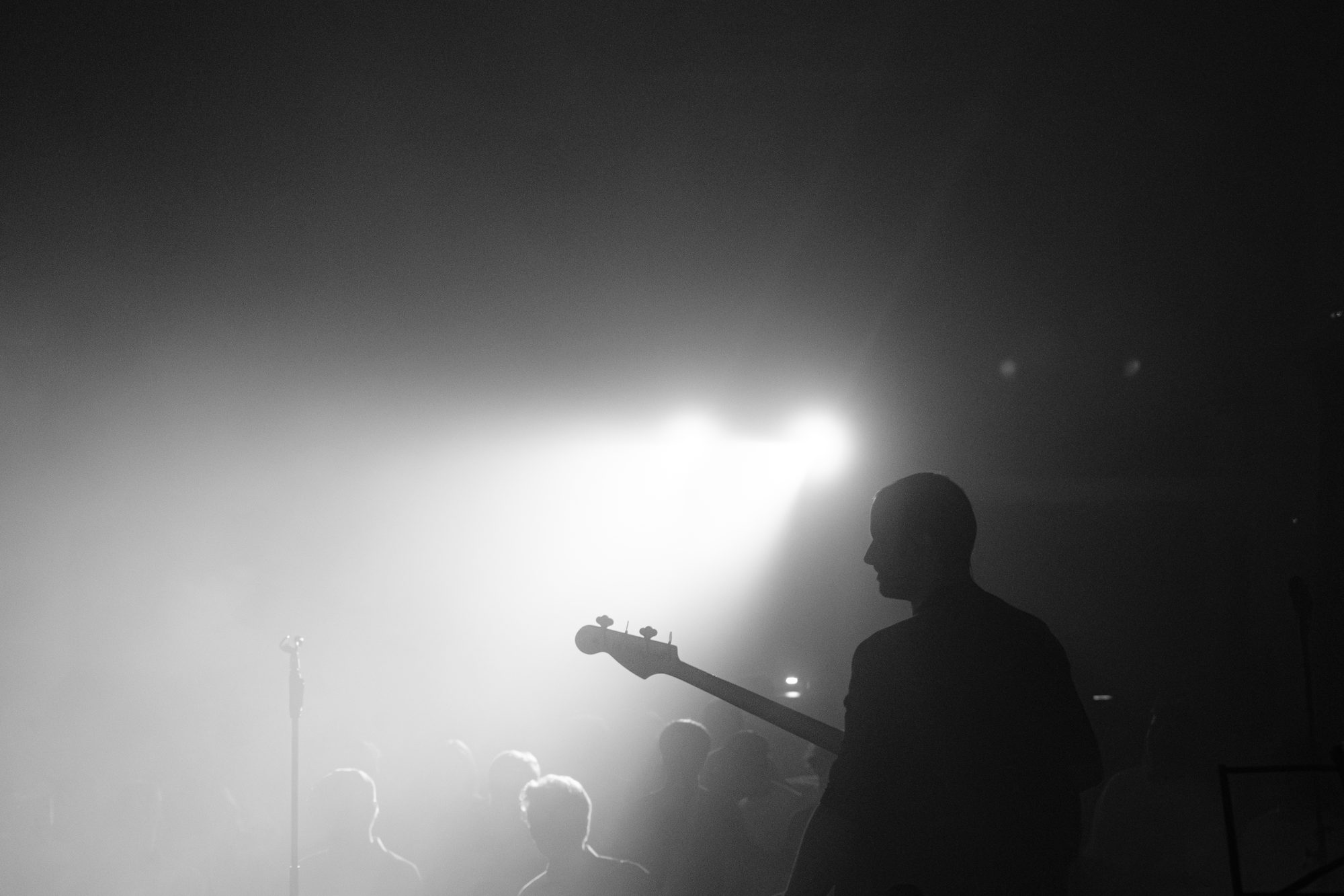 A bass player in silhouette against stage fog and one hard beam of light.