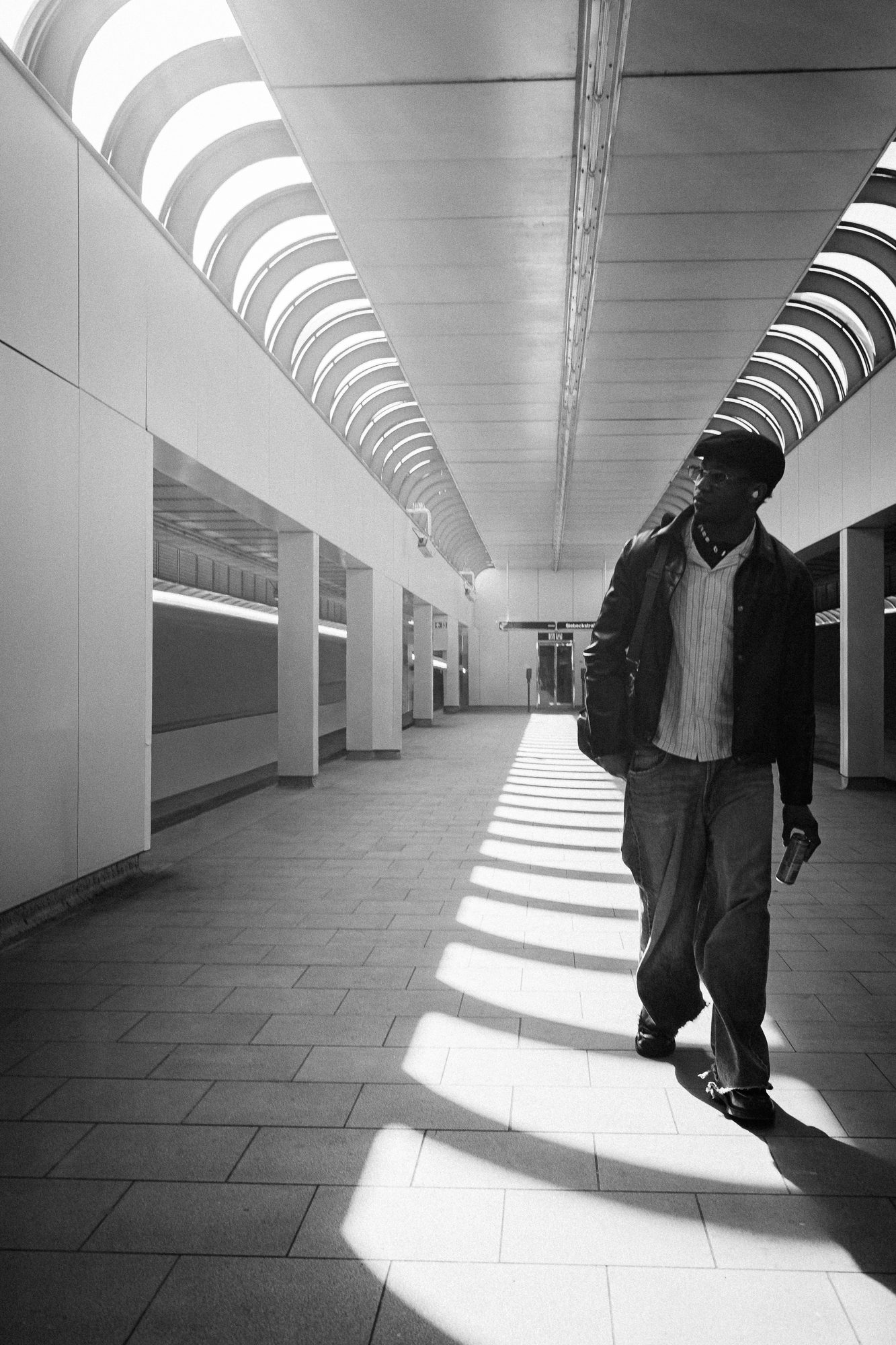 A man walks through an underpass, stripes of light and shadow across the floor.