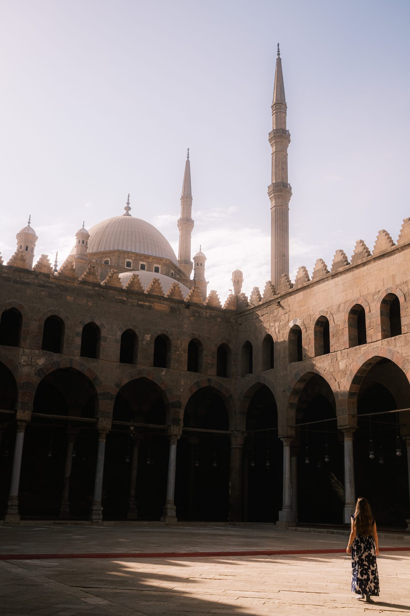 A woman walks alone through the arcaded courtyard of a mosque.