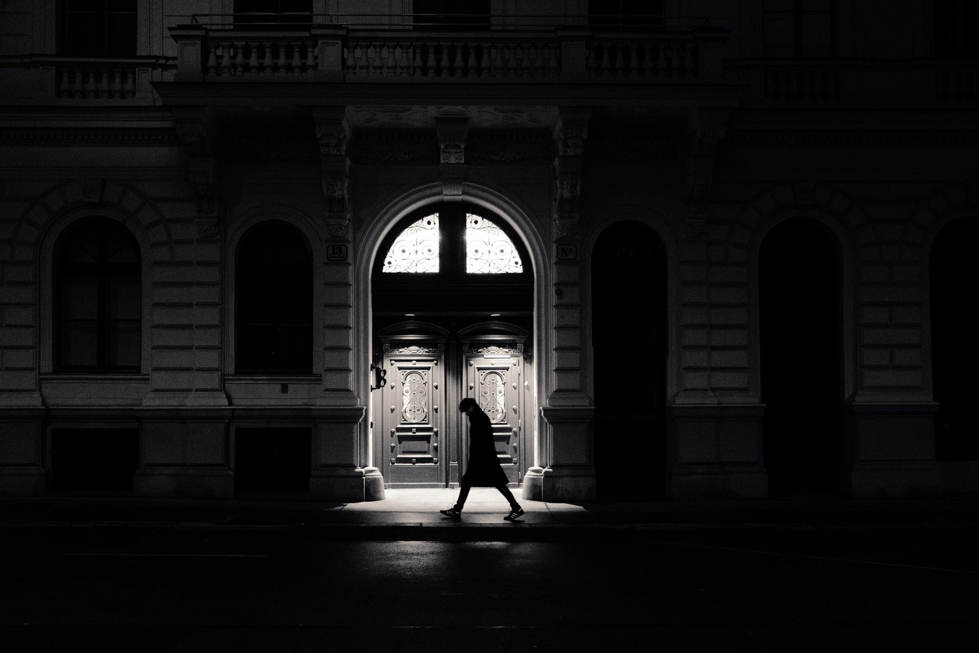 A silhouette passes a lit palace doorway at night, the street around it black.