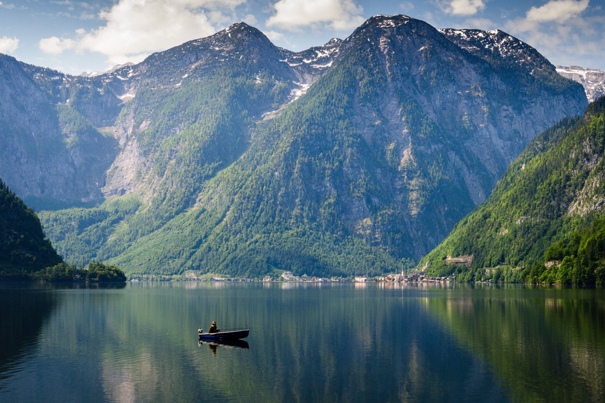A lone fisherman in a small boat on Lake Hallstatt below steep green mountains.