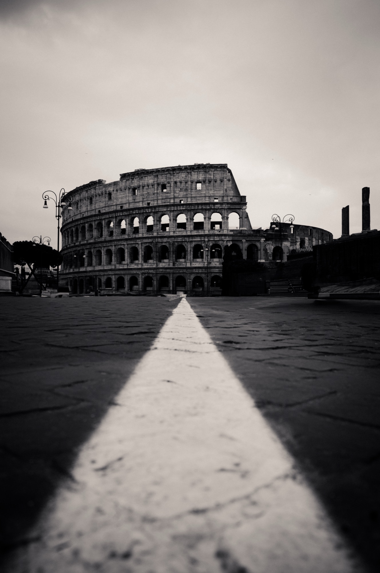 The Colosseum in black and white, seen low along a white line across the pavement.