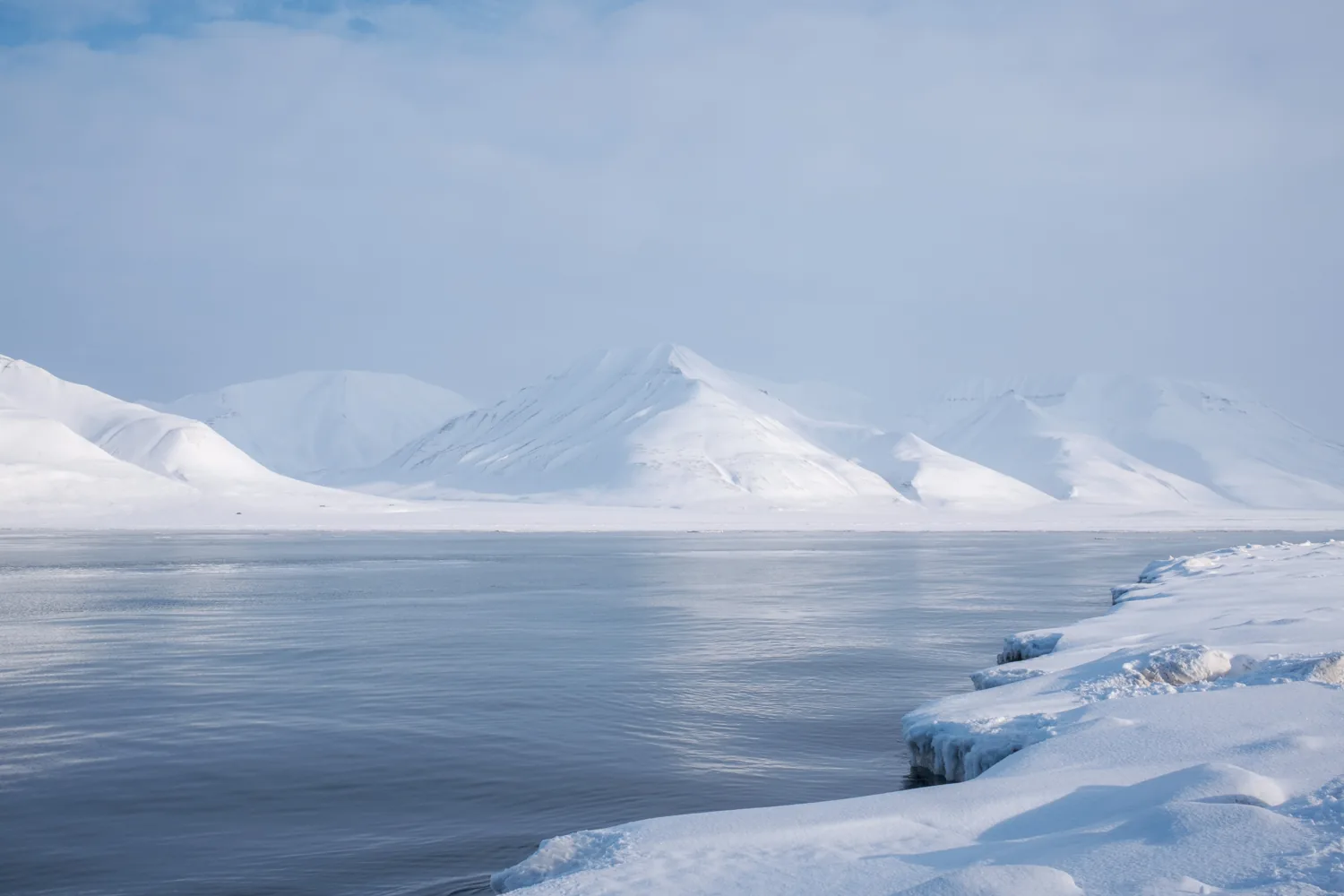 A frozen sea in front of low mountains, still and quiet.
