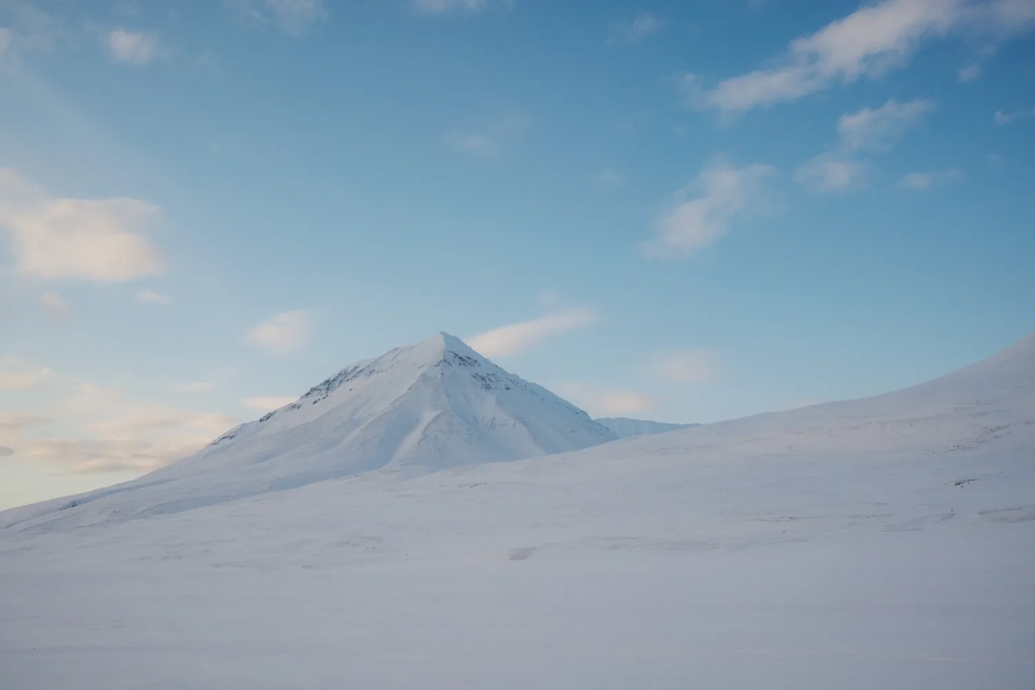 A pyramid-shaped mountain rises from a smooth field of snow.