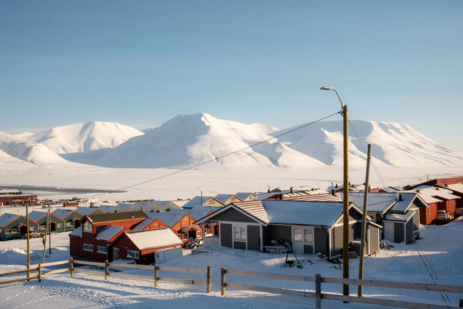 Rows of colourful wooden houses below snow-covered mountains, a street lamp in the foreground.