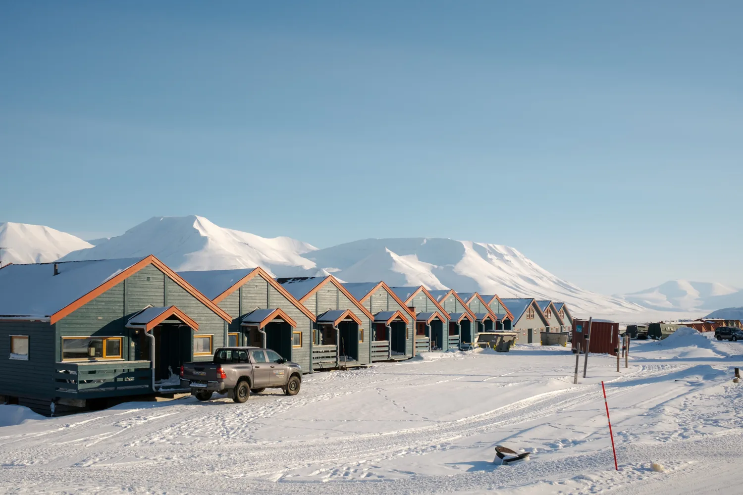 A row of small colourful cabins in the snow, mountains behind under a clear sky.