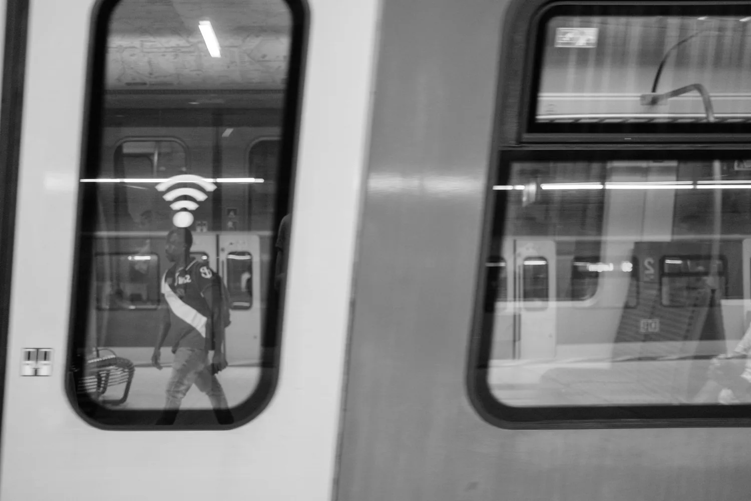 A reflection in a train window, a person passing, a wifi symbol beside them.