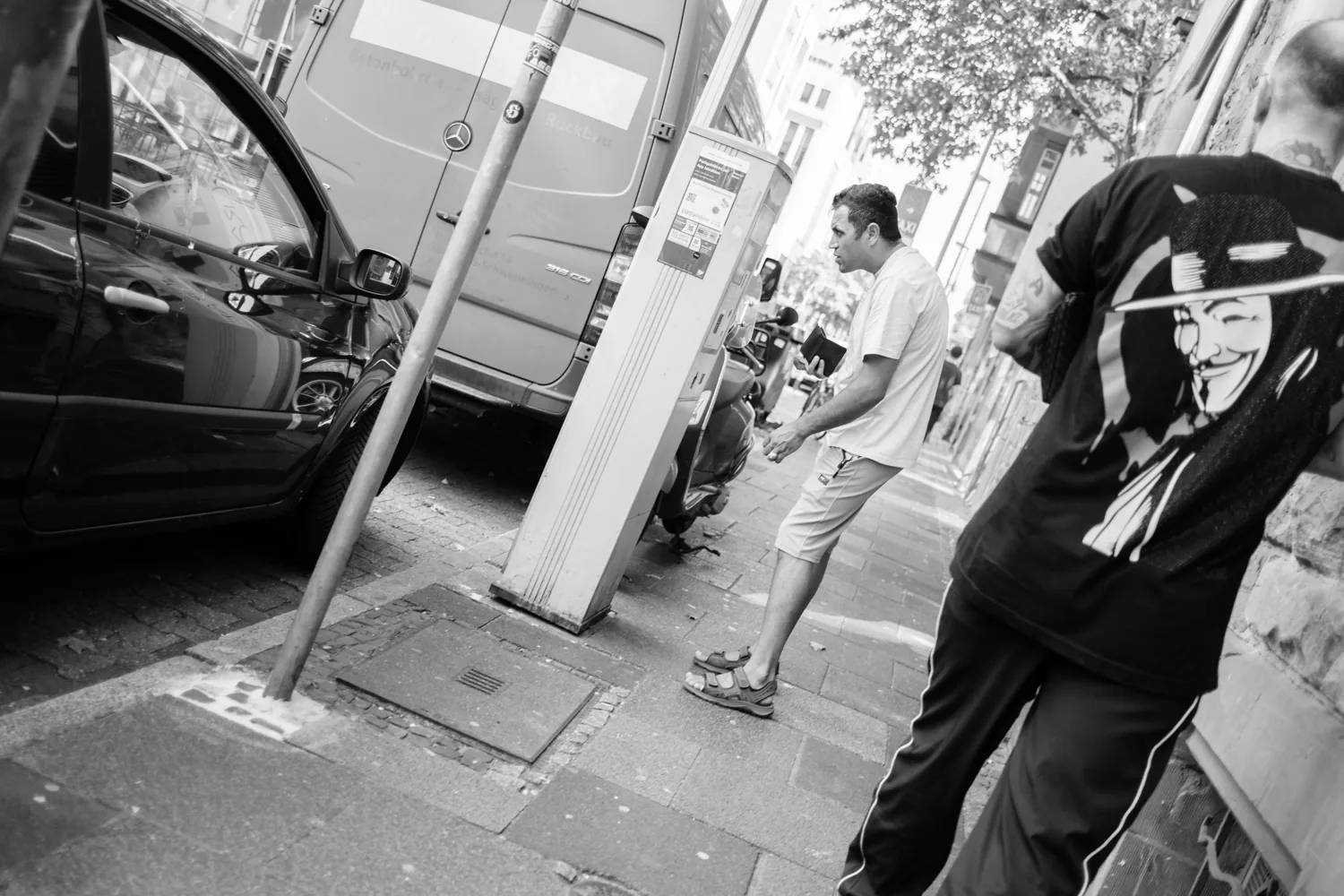 A street scene, a man bending down beside a parked van.
