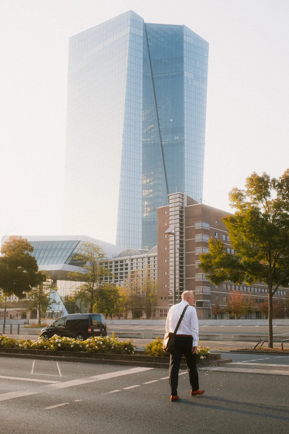 A businessman crosses an empty street in front of a large modern building.