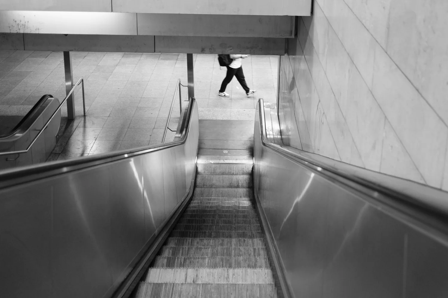 A tiny figure at the top of an escalator, seen from far below.