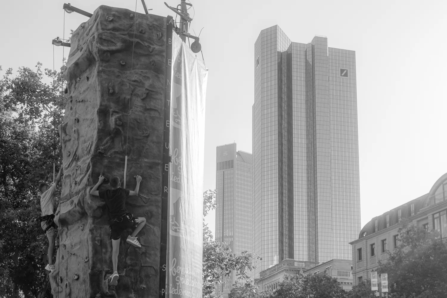 A colourful climbing wall stands in front of the glass bank towers.