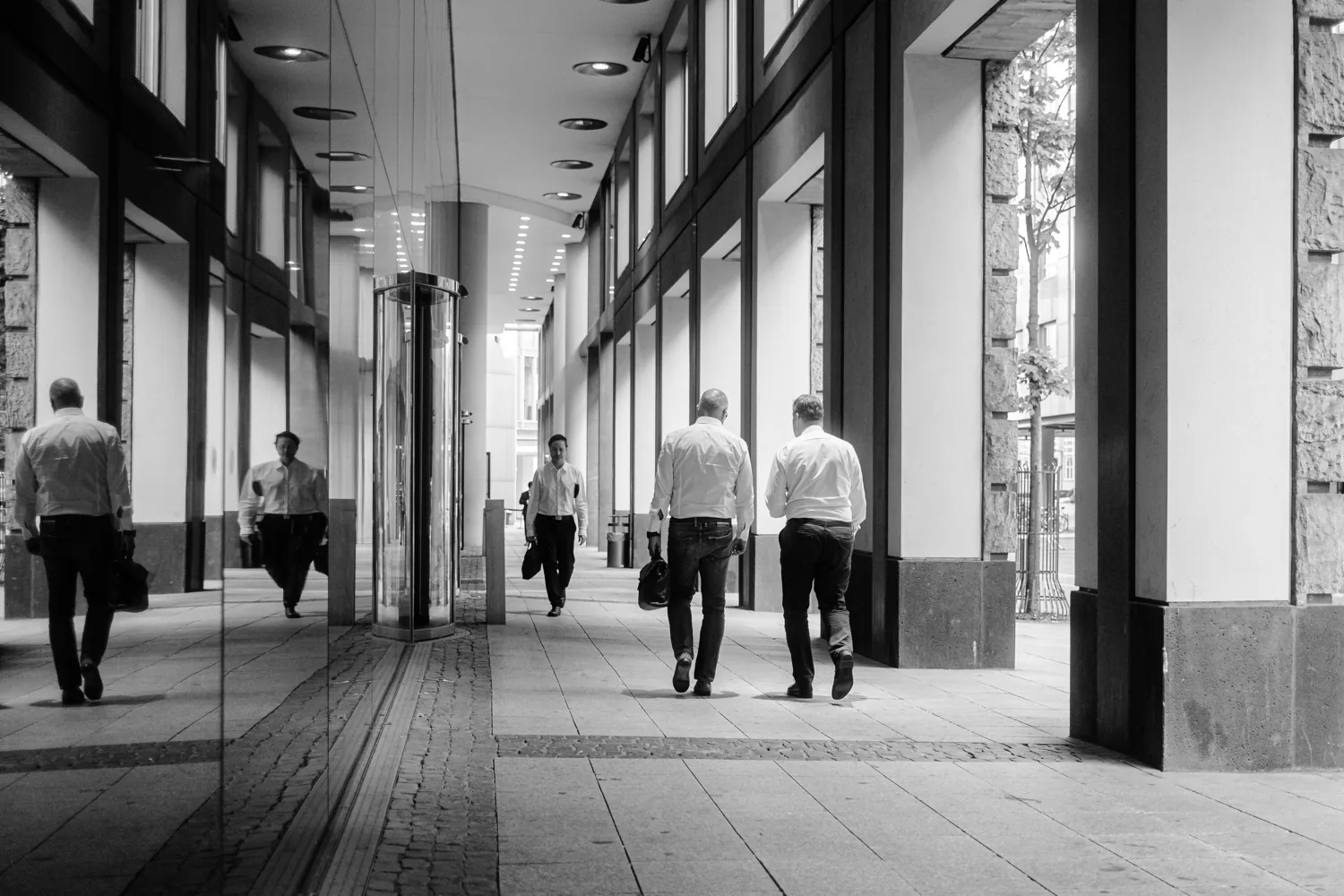 Men in suits walk away through an empty arcade.