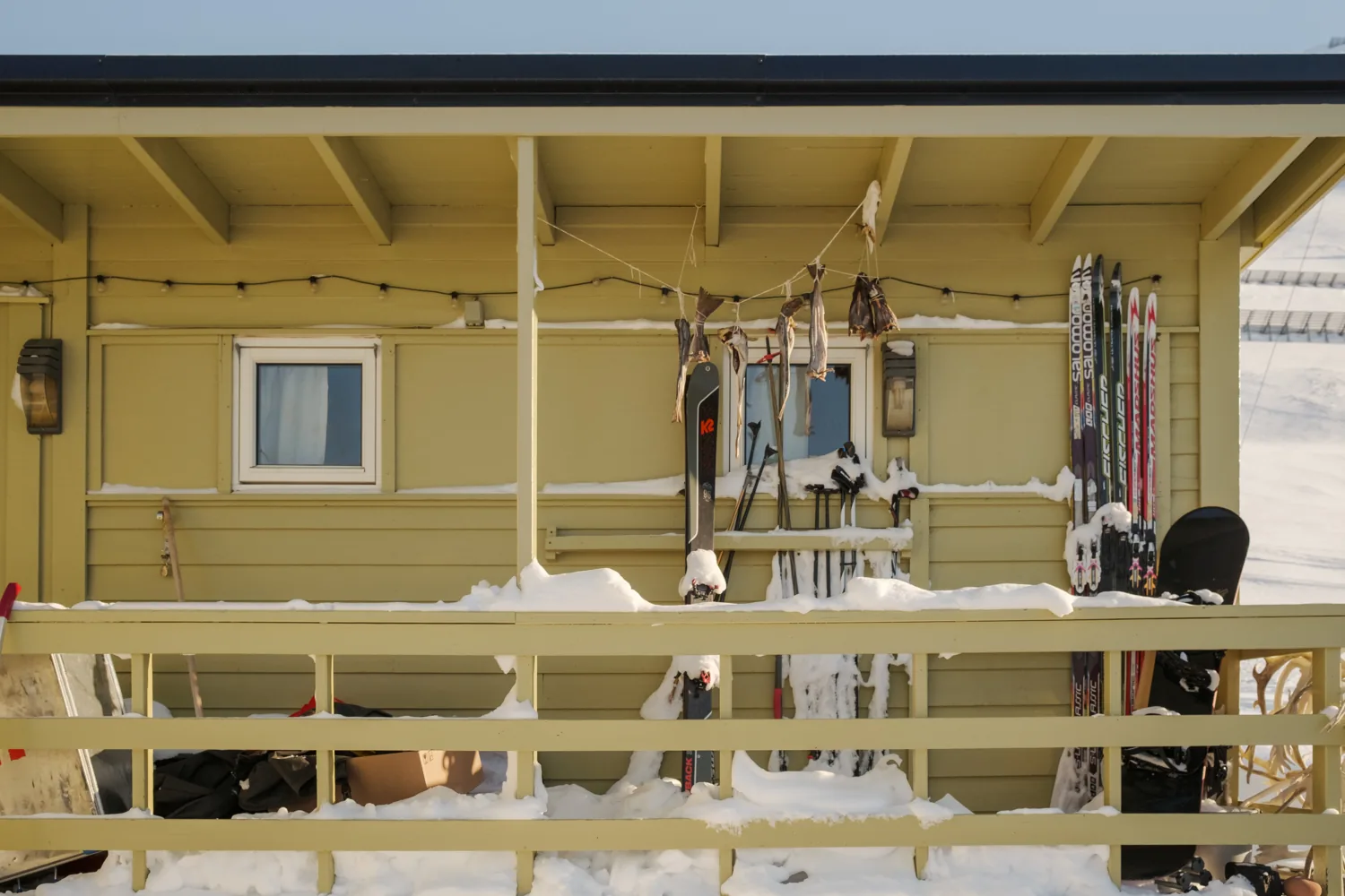 A house veranda hung with skis, gear and drying clothes above the snow.