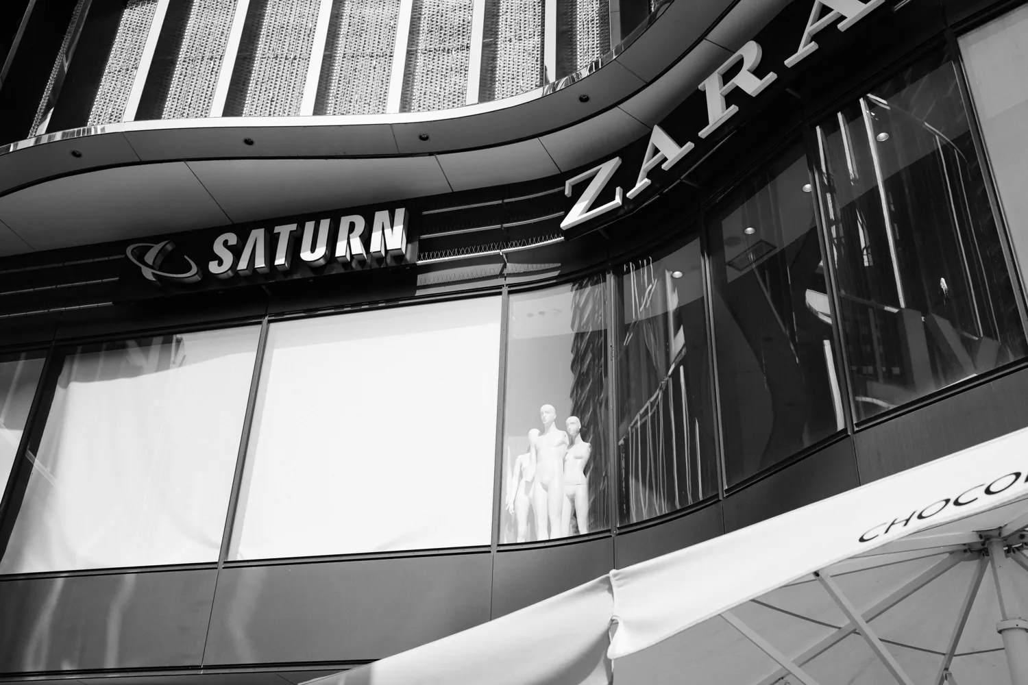 Shop windows of Saturn and Zara curve along a city street.