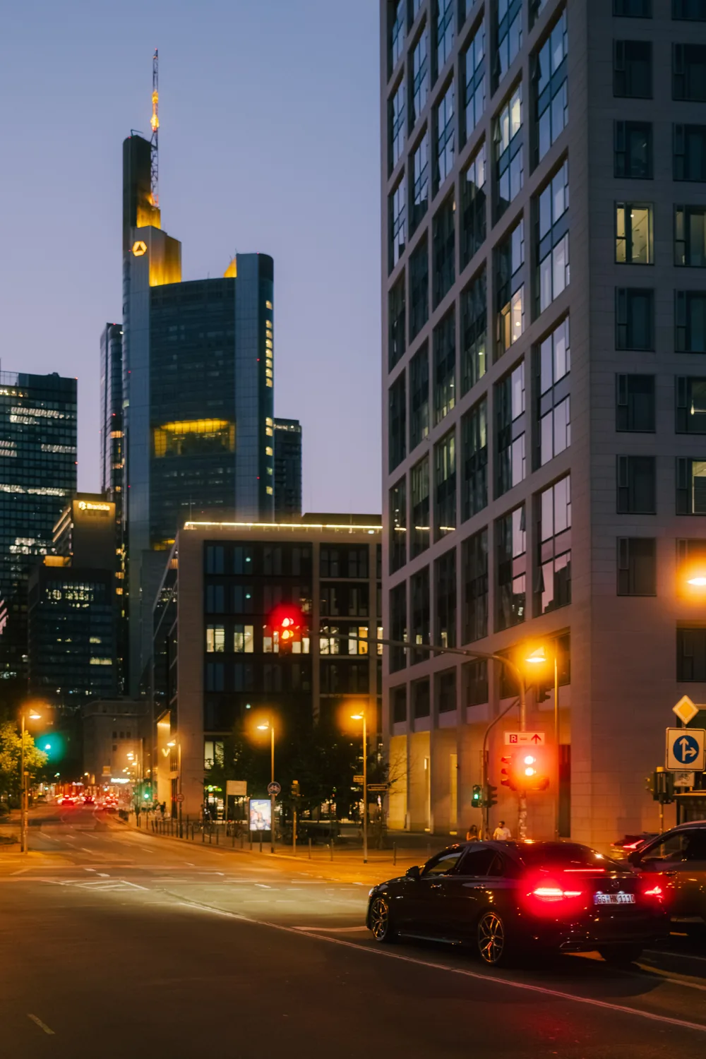 A night street with traffic lights and red tail-lights, office buildings behind.