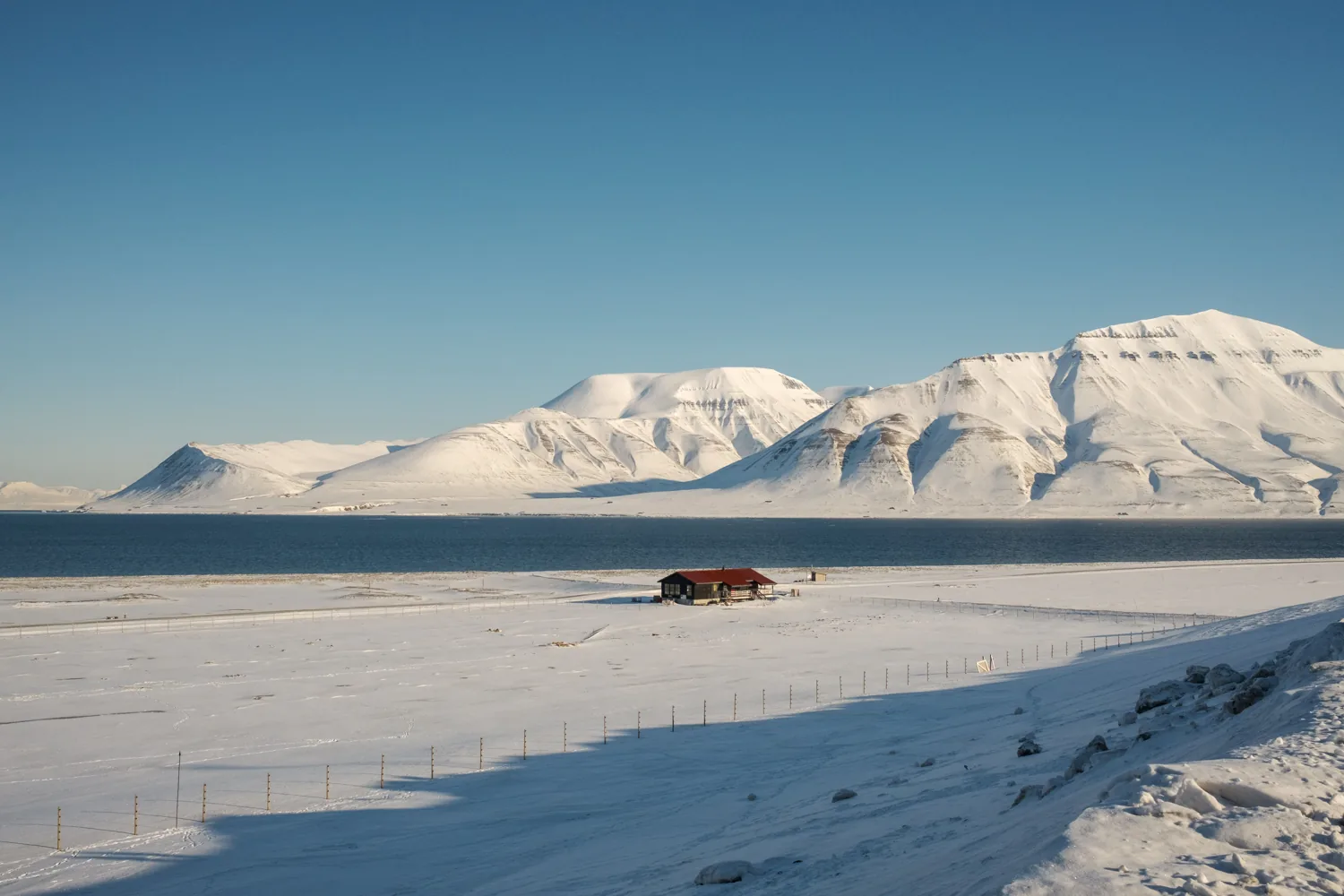 A small red car on a wide snowfield below distant mountains.