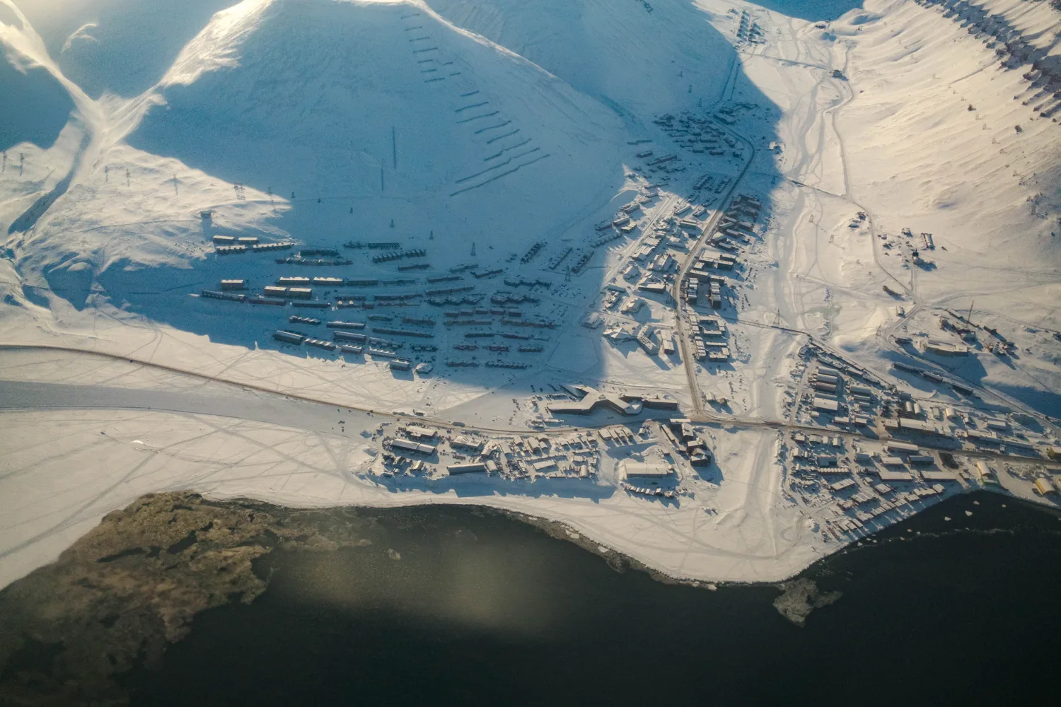Aerial view of Longyearbyen, a small colourful town on a fjord ringed by snow-covered mountains.