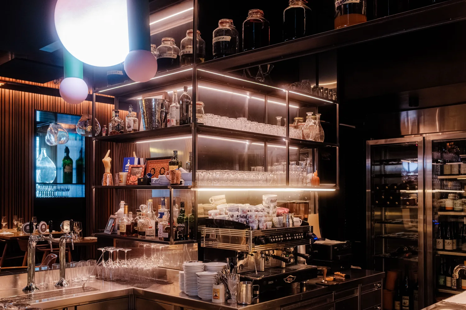 The warmly lit back bar of a restaurant, shelves of bottles and glasses.
