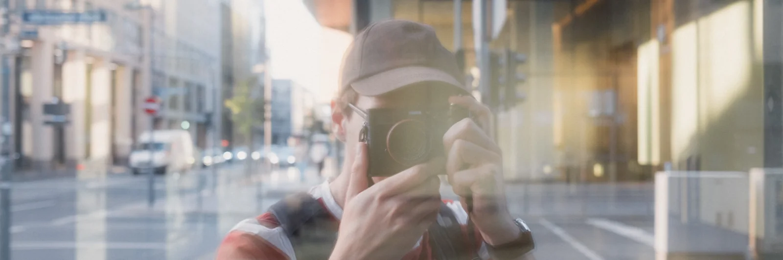 Lukas Mari photographing, reflected in a shop window with the city street behind him.